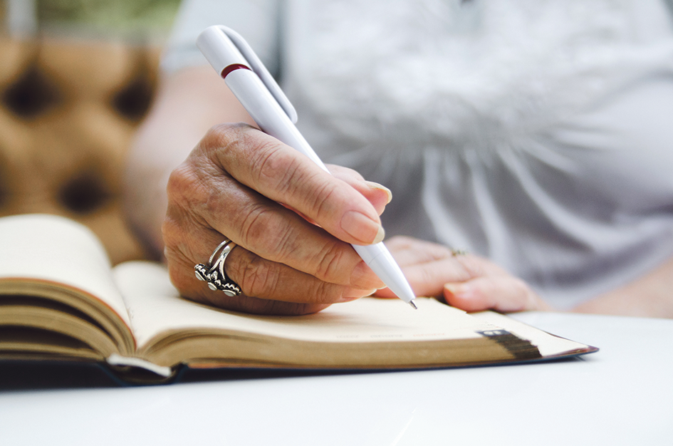 Eine Frauenhand mit einem Ring schreibt mit einem Kugelschreiberstift etwas in ein Buch.